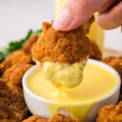 Keto chicken nugget being dipped in honey mustard dressing.
