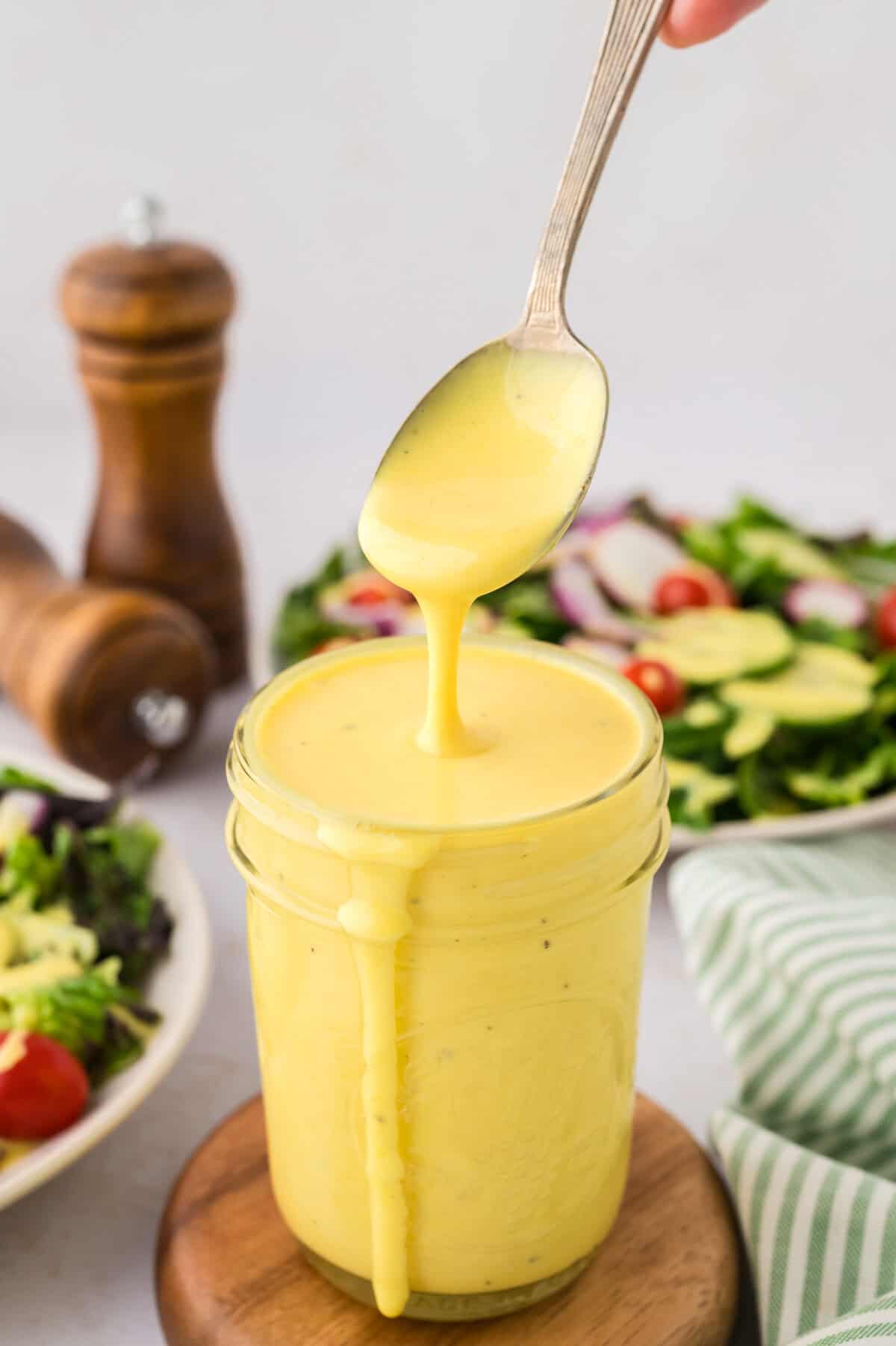 Keto honey mustard dripping off a spoon into a mason jar.