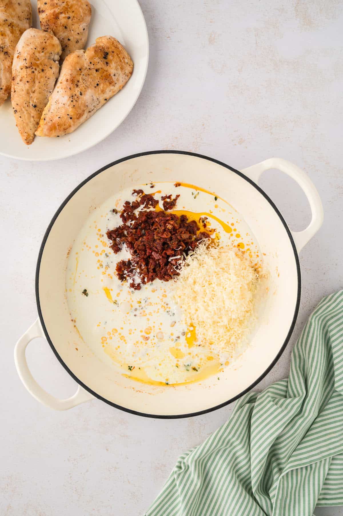Sun-dried tomatoes, parmesan, and cream in skillet to make a pan sauce for keto marry me chicken.
