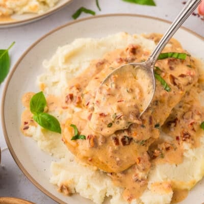 Sun-dried tomato cream sauce being spooned over chicken.