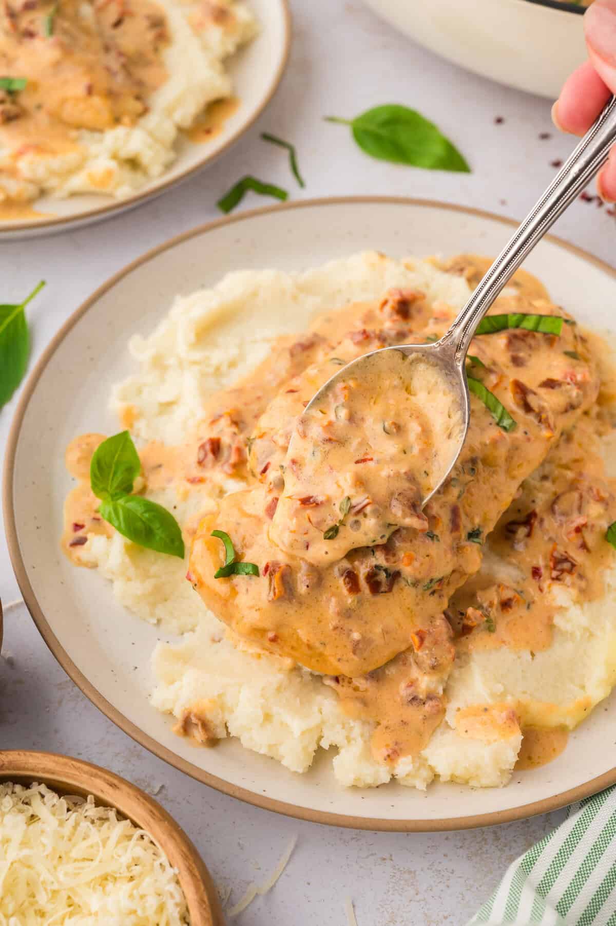 Sun-dried tomato cream sauce being spooned over chicken.
