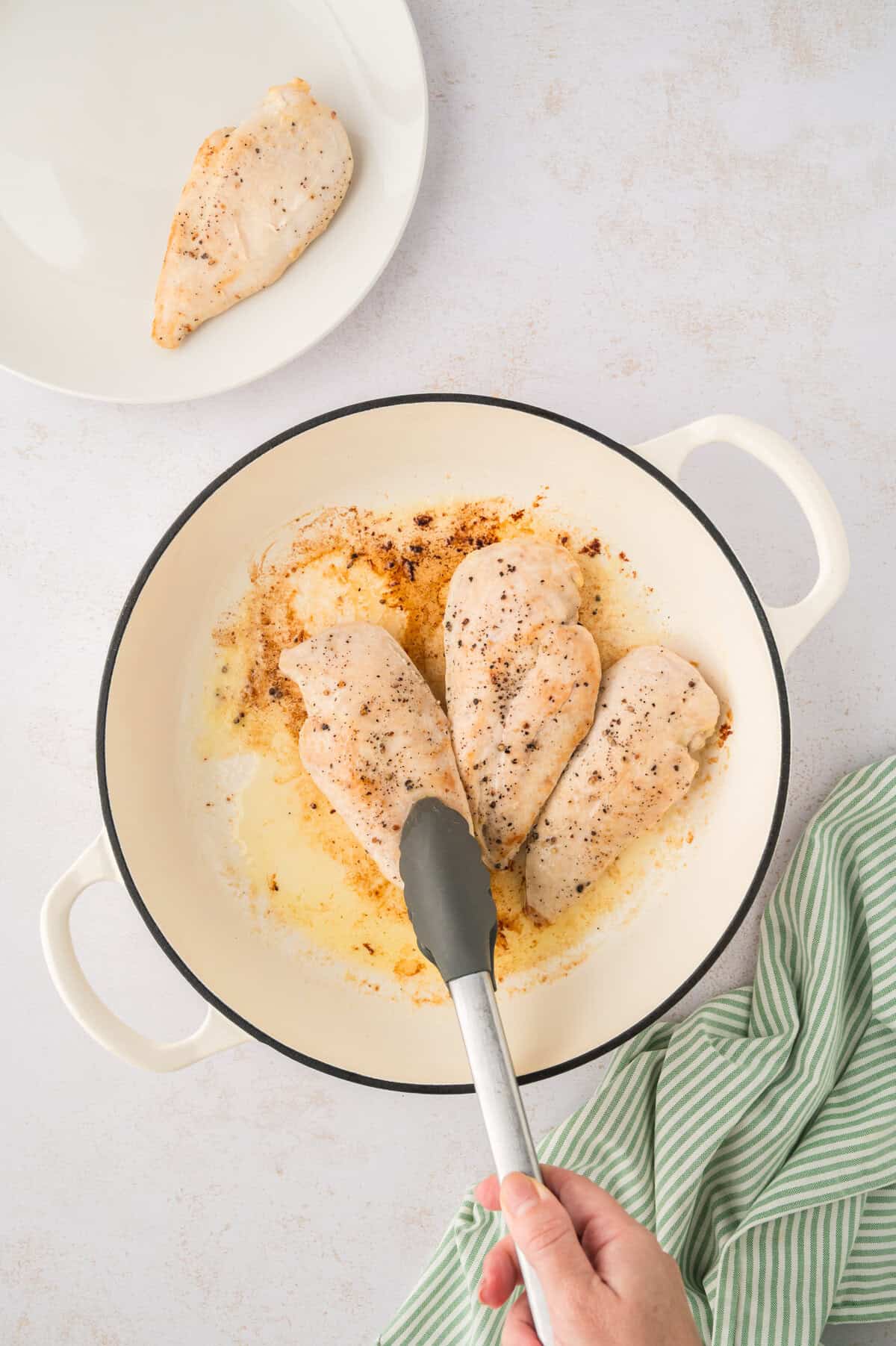 Seasoned chicken breasts being seared in a skillet.