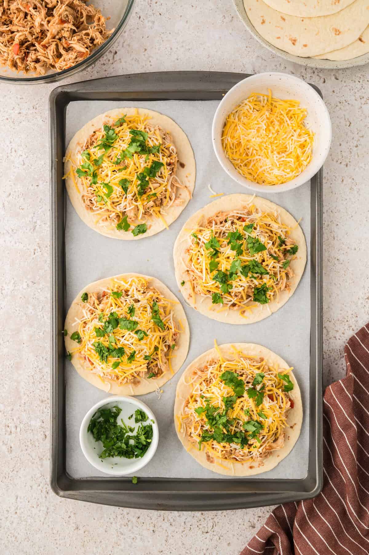 Chicken, cheese, and cilantro on low carb tortillas on sheet pan.