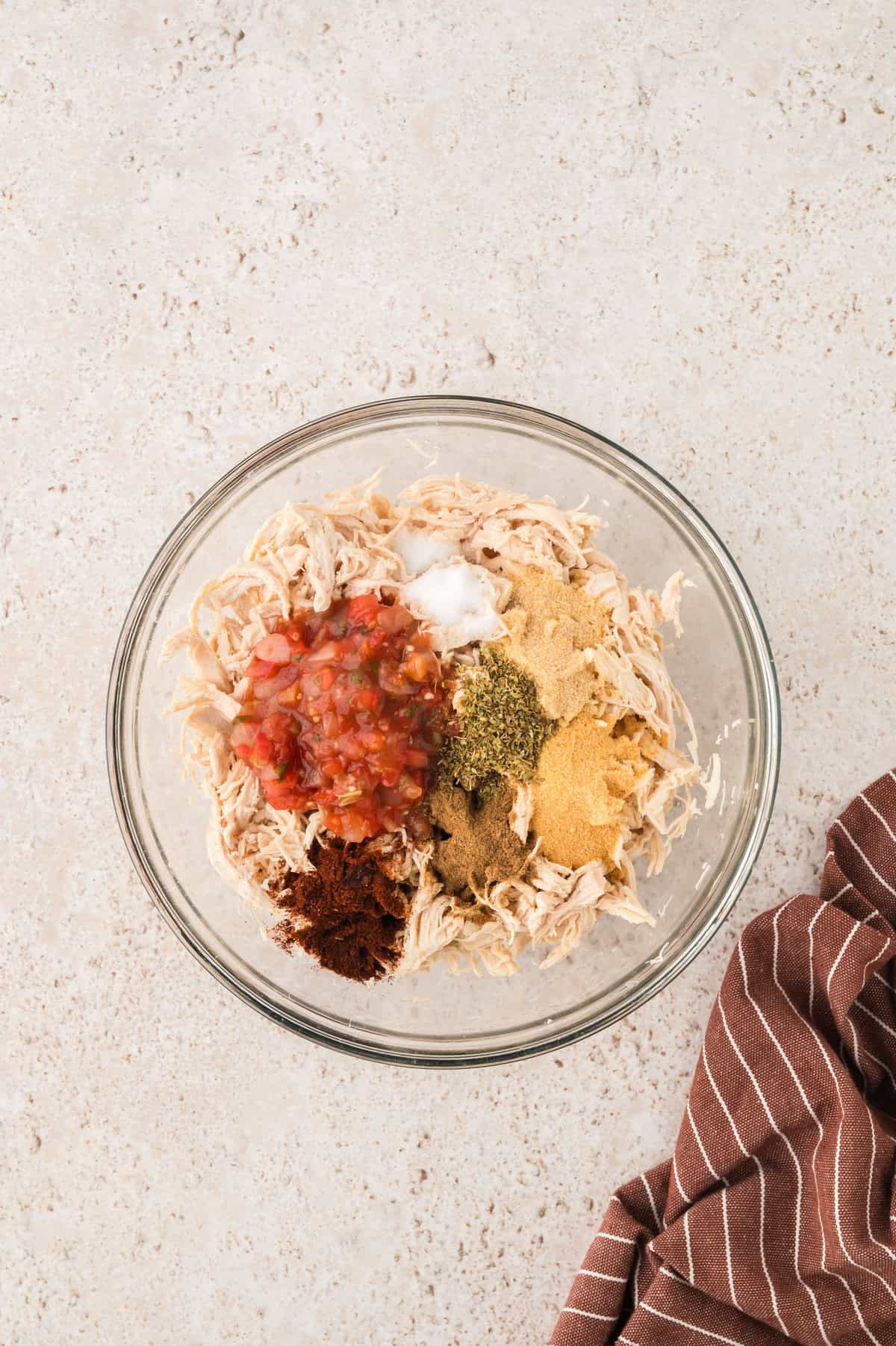 Shredded chicken in mixing bowl with seasonings and salsa.