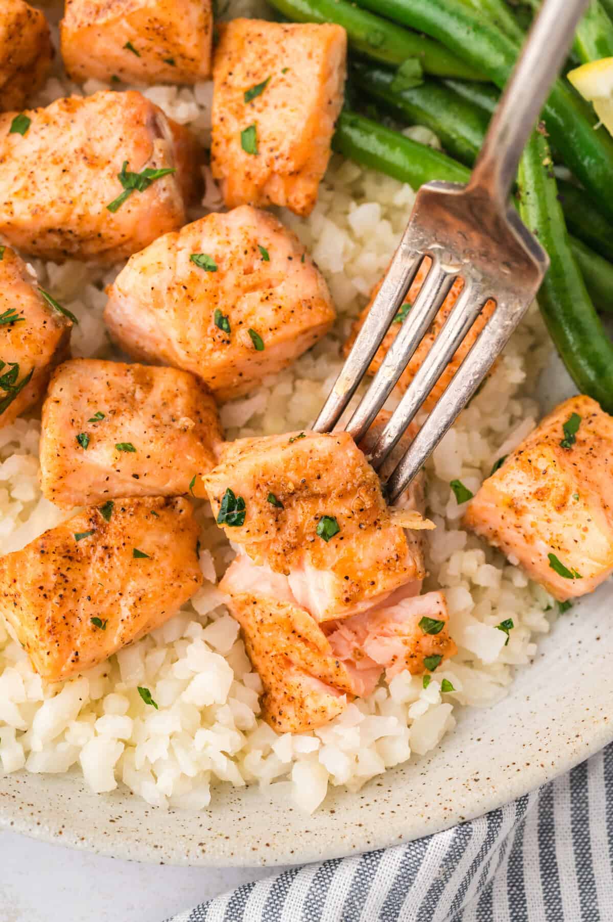 Keto salmon bite on fork with cauliflower rice and green beans.