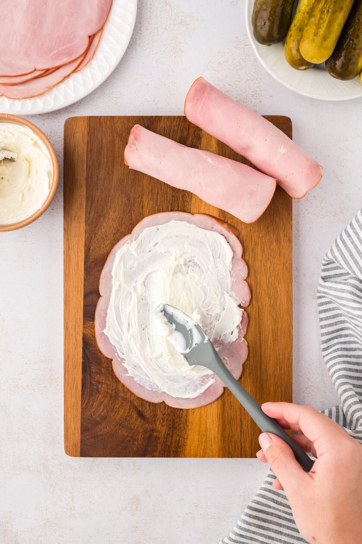 Deli ham being spread with cream cheese.