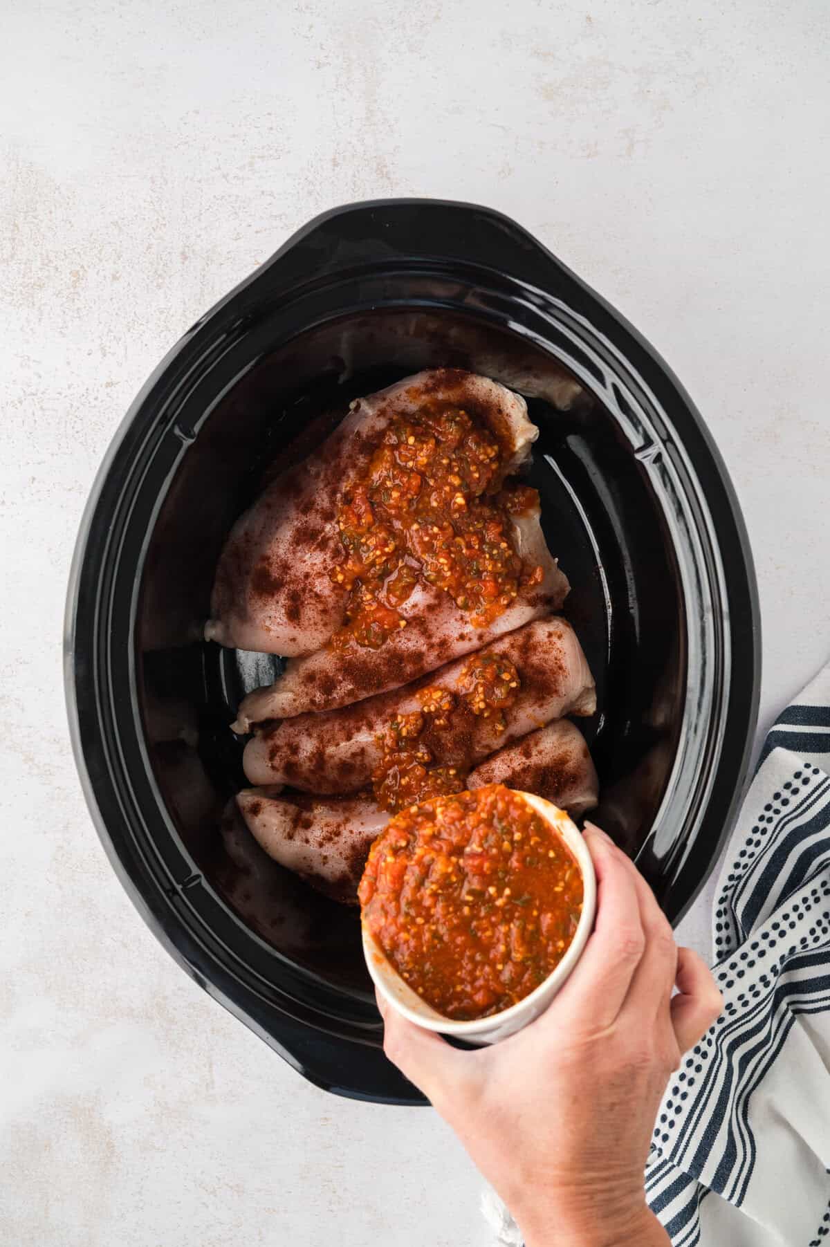 Salsa being poured over chicken in crockpot.