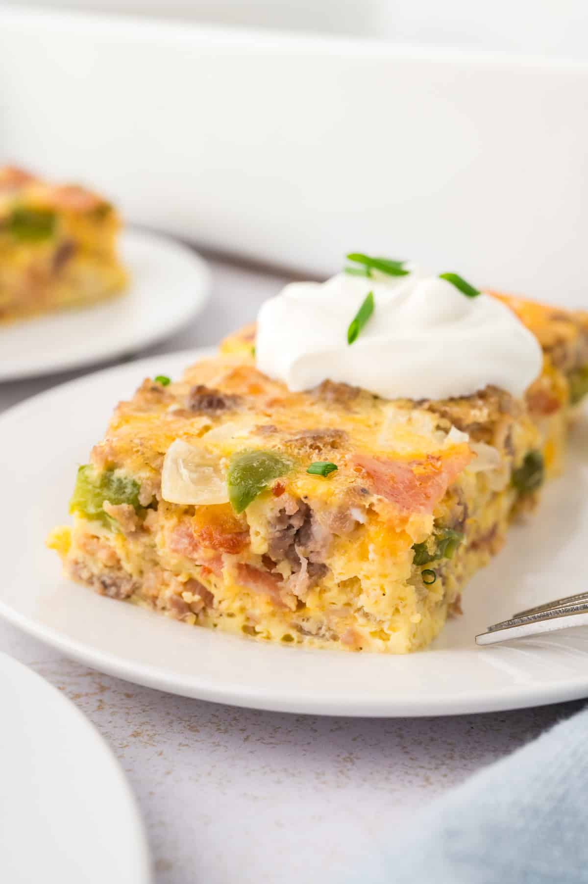 Low carb breakfast casserole sliced on a plate and topped with sour cream.