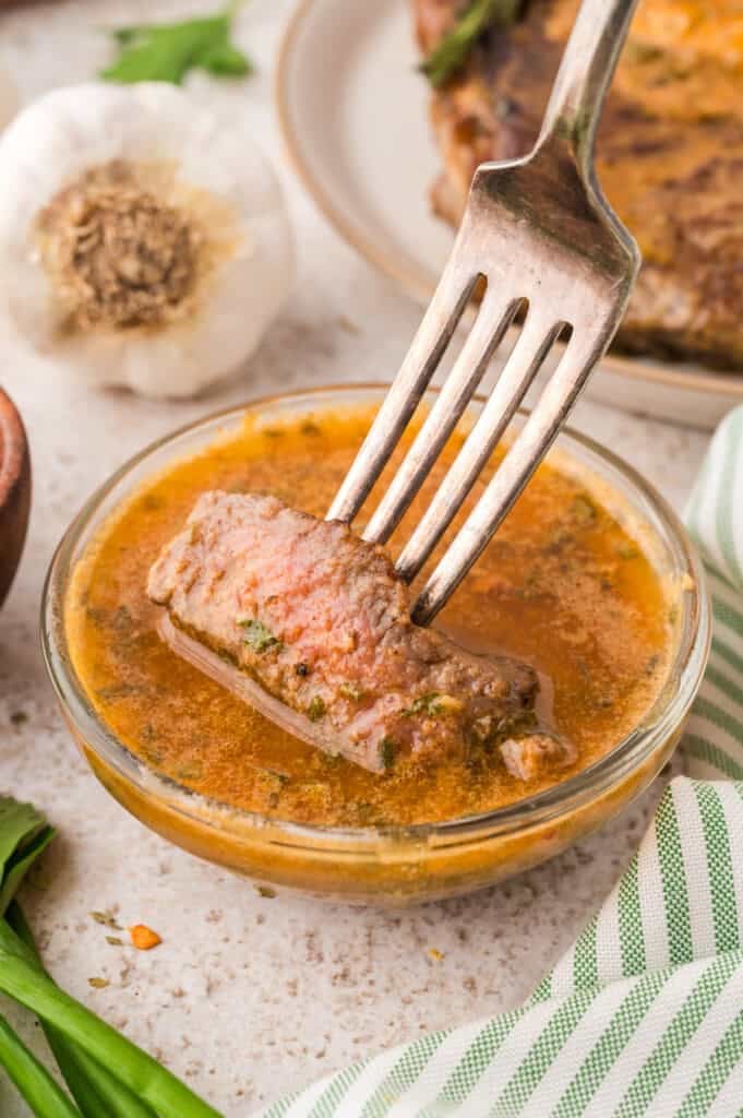 A piece of steak being dipped into cowboy butter.