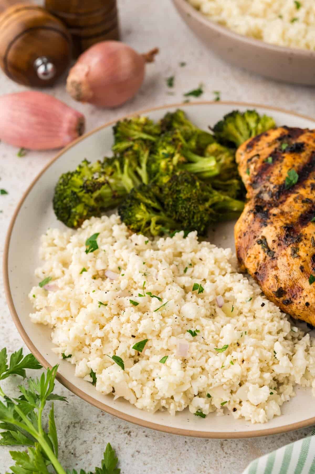 Cauliflower rice pilaf on plate with grilled chicken and broccoli.