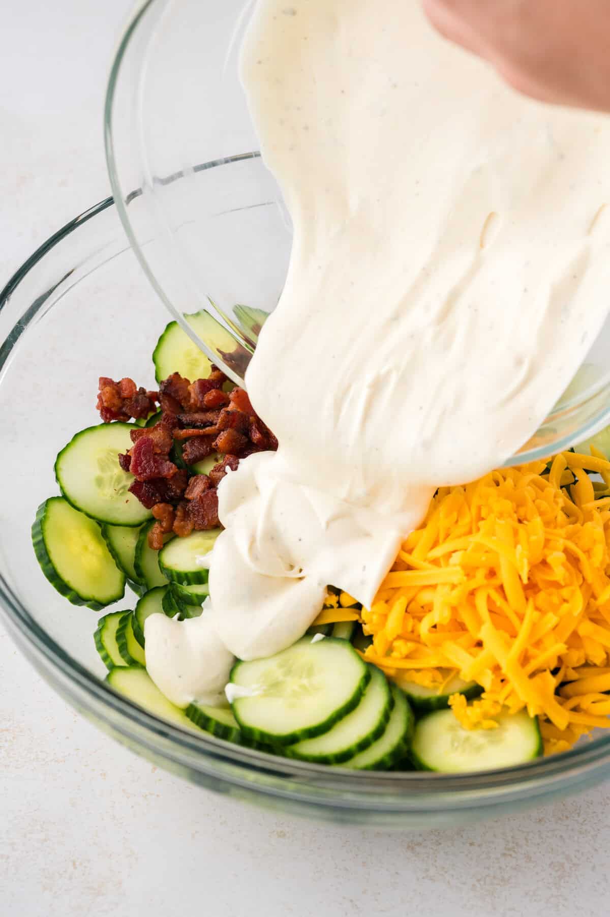 Ranch dressing being poured over cucumber salad.