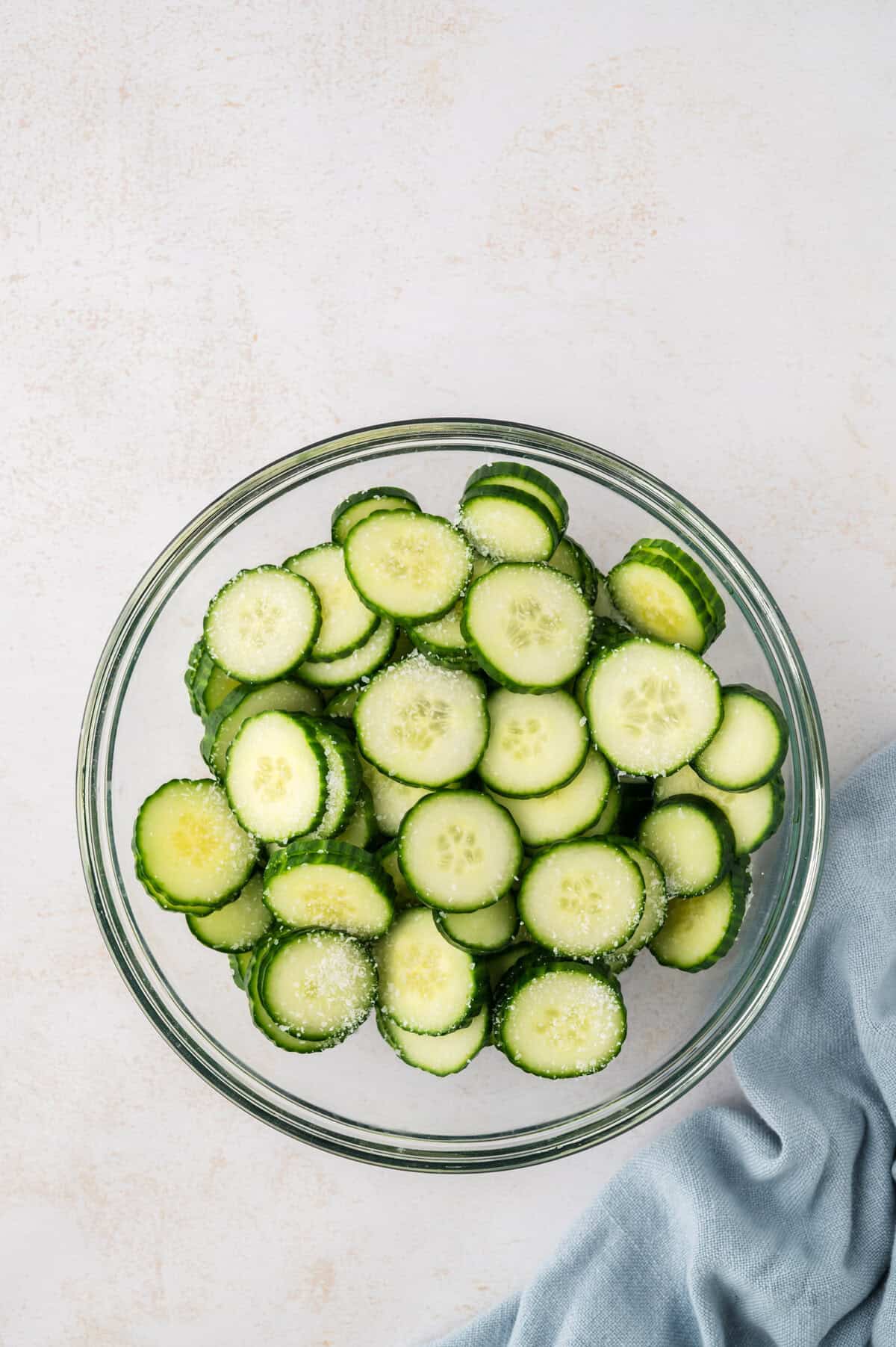 Sliced cucumbers in bowl with salt.