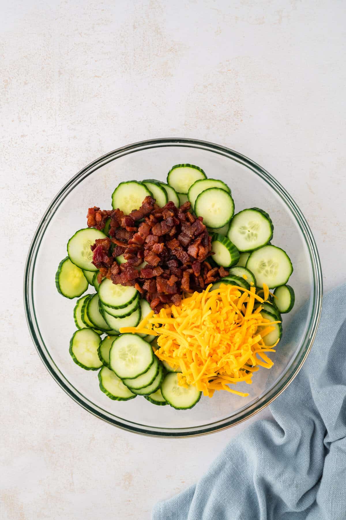 Bacon and cheddar in bowl with sliced cucumbers.