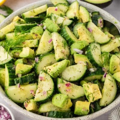 Bowl filled with cucumbers, avocado, red onions, and dressing.