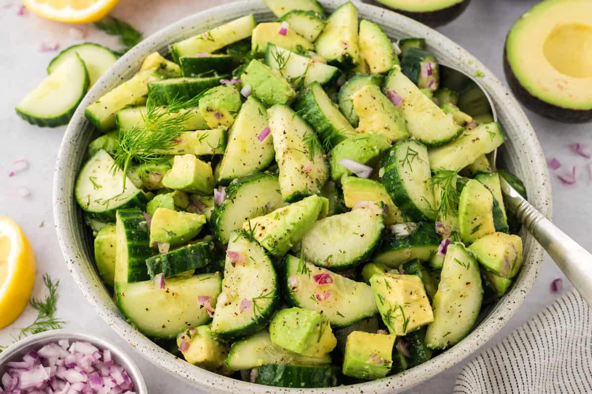 Bowl filled with cucumbers, avocado, red onions, and dressing.