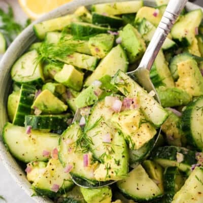 Serving spoon full of cucumber avocado salad recipe over serving dish.