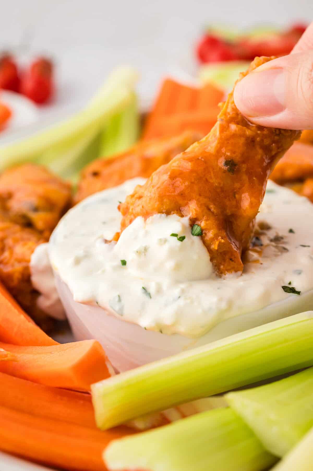 Buffalo wing being dunked in keto blue cheese dressing.
