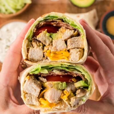Hands holding a chicken club wrap in a low carb tortilla.
