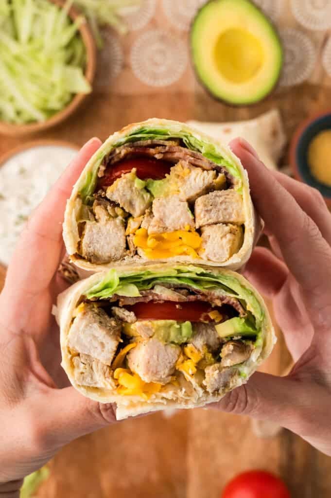 Hands holding a chicken club wrap in a low carb tortilla.