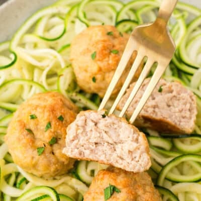 Baked chicken meatball on fork over zucchini.