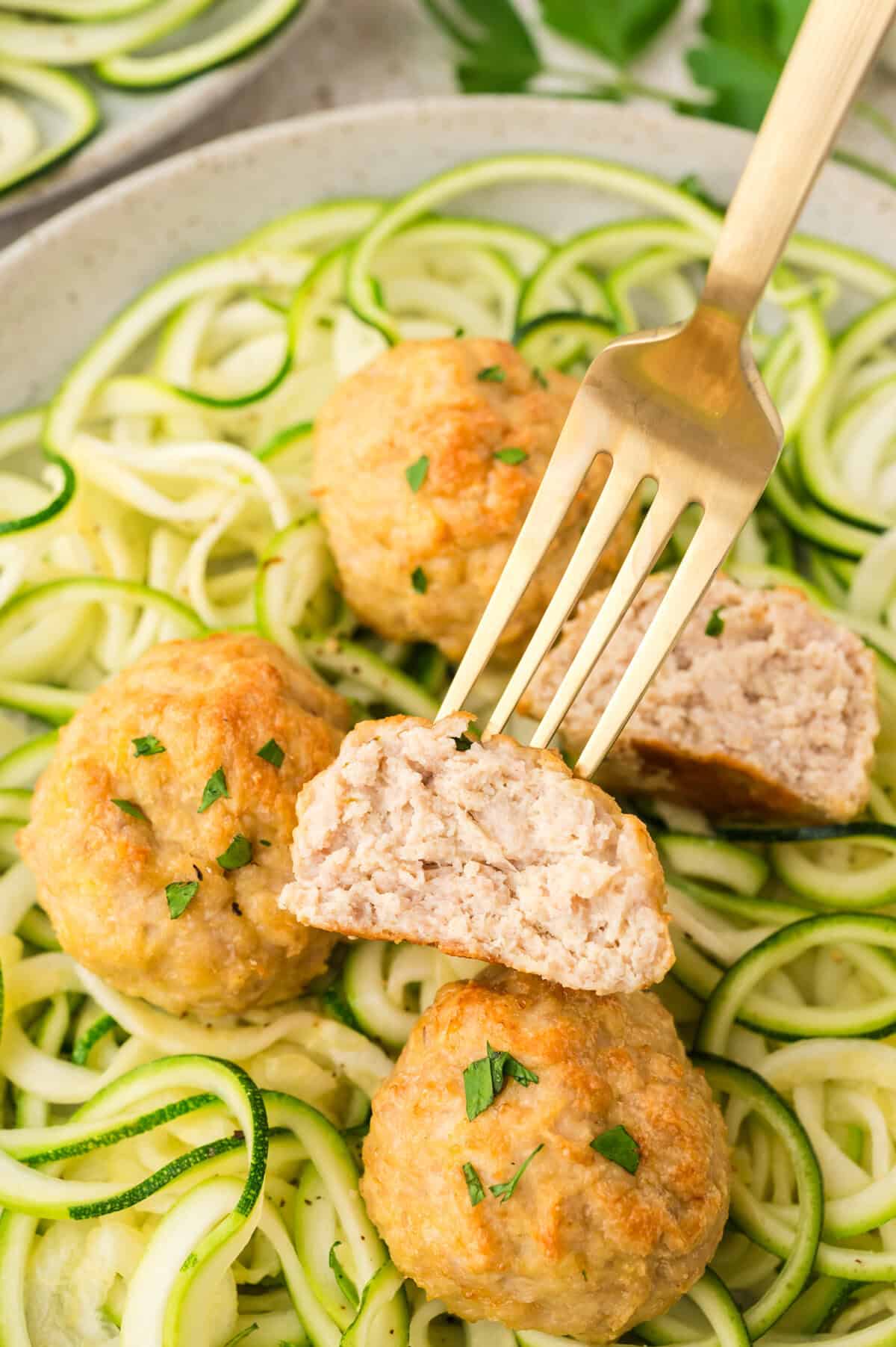Baked chicken meatball on fork over zucchini.