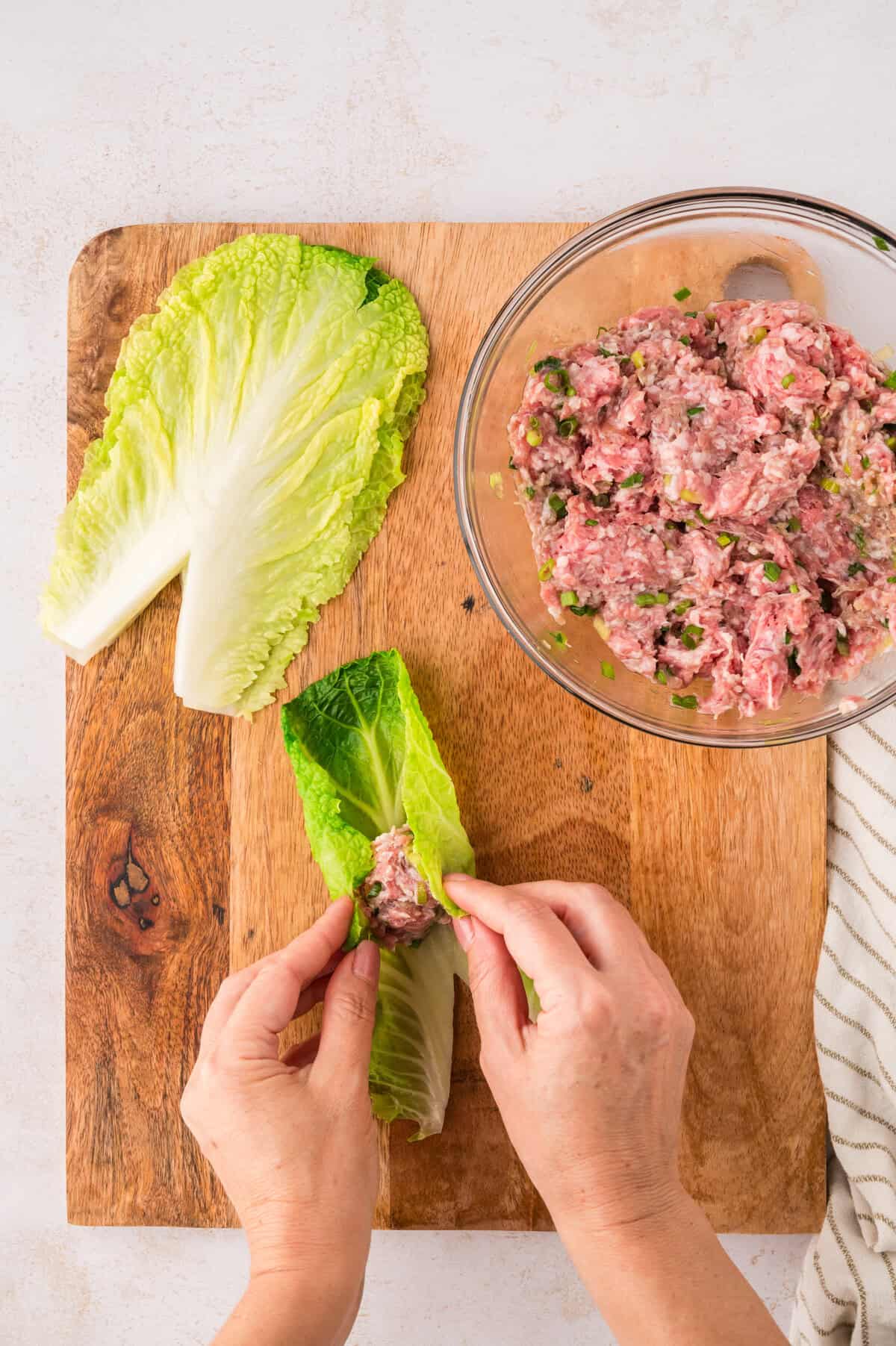 Pork being rolled up in cabbage leaves.