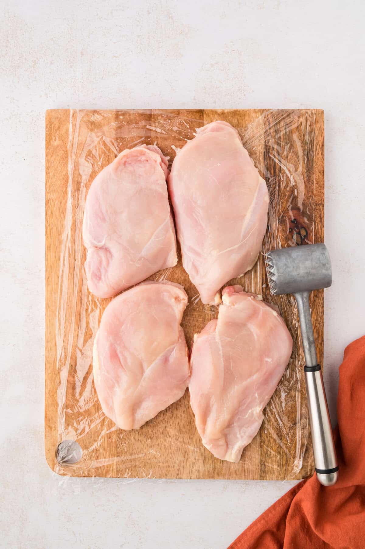Chicken breasts being pounded to an even thickness.