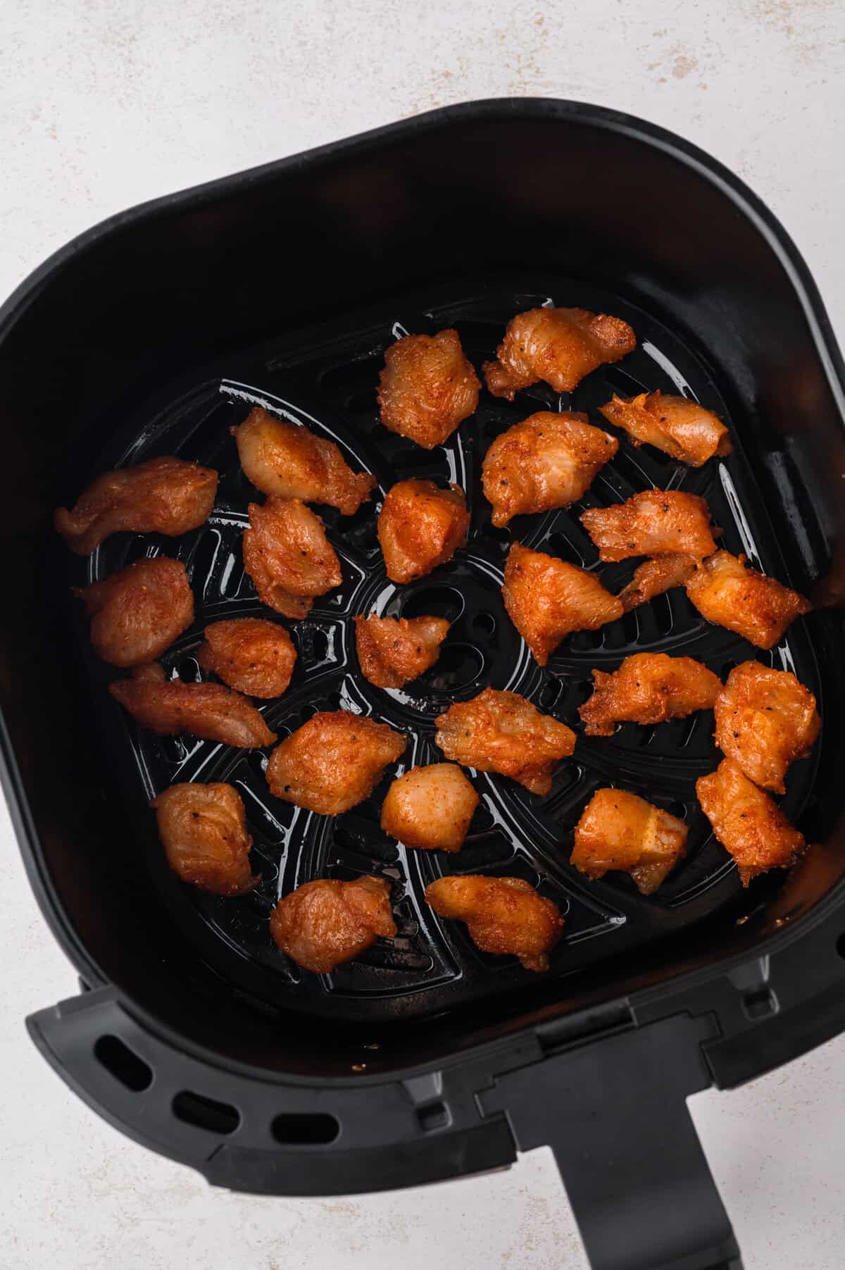 Seasoned chicken in air fryer basket.