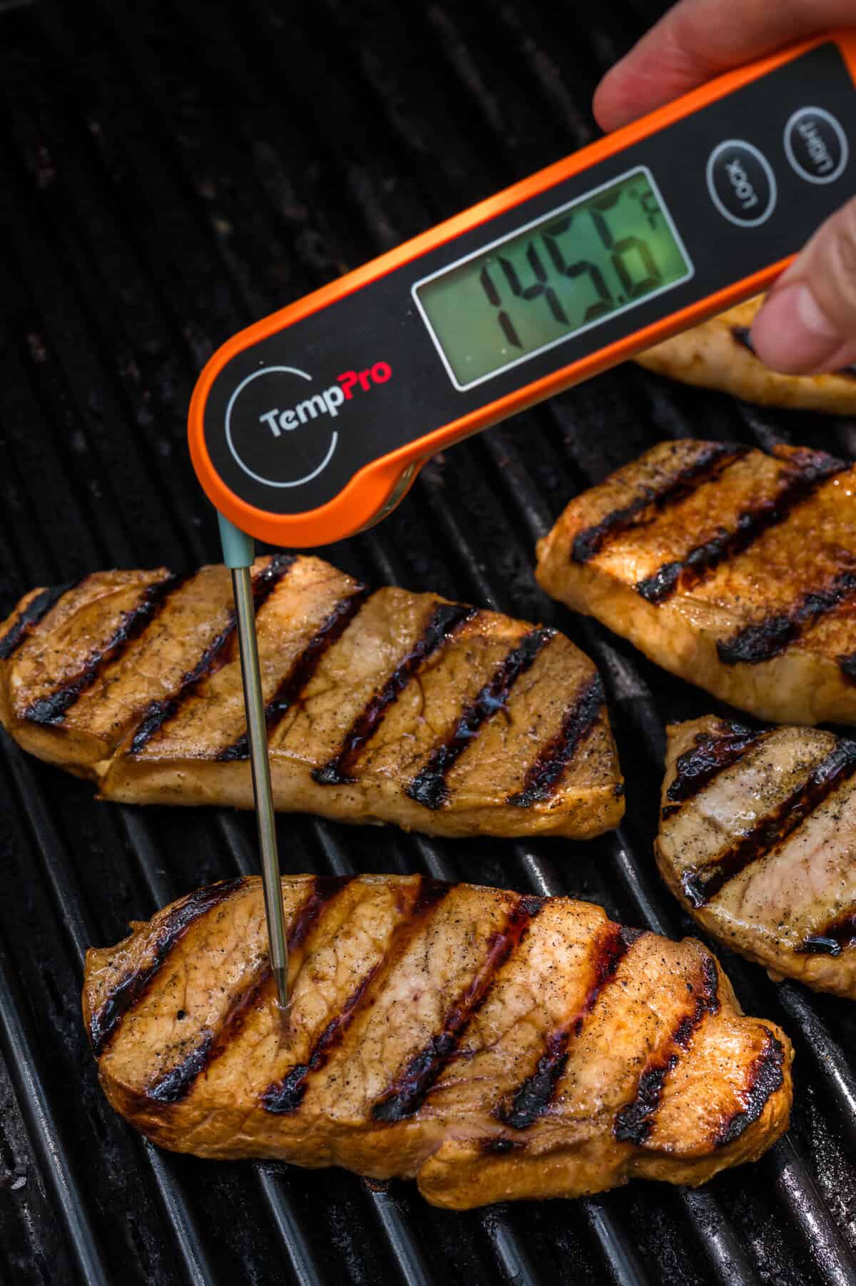 Pork chops on a grill being cooked to 145 degrees.