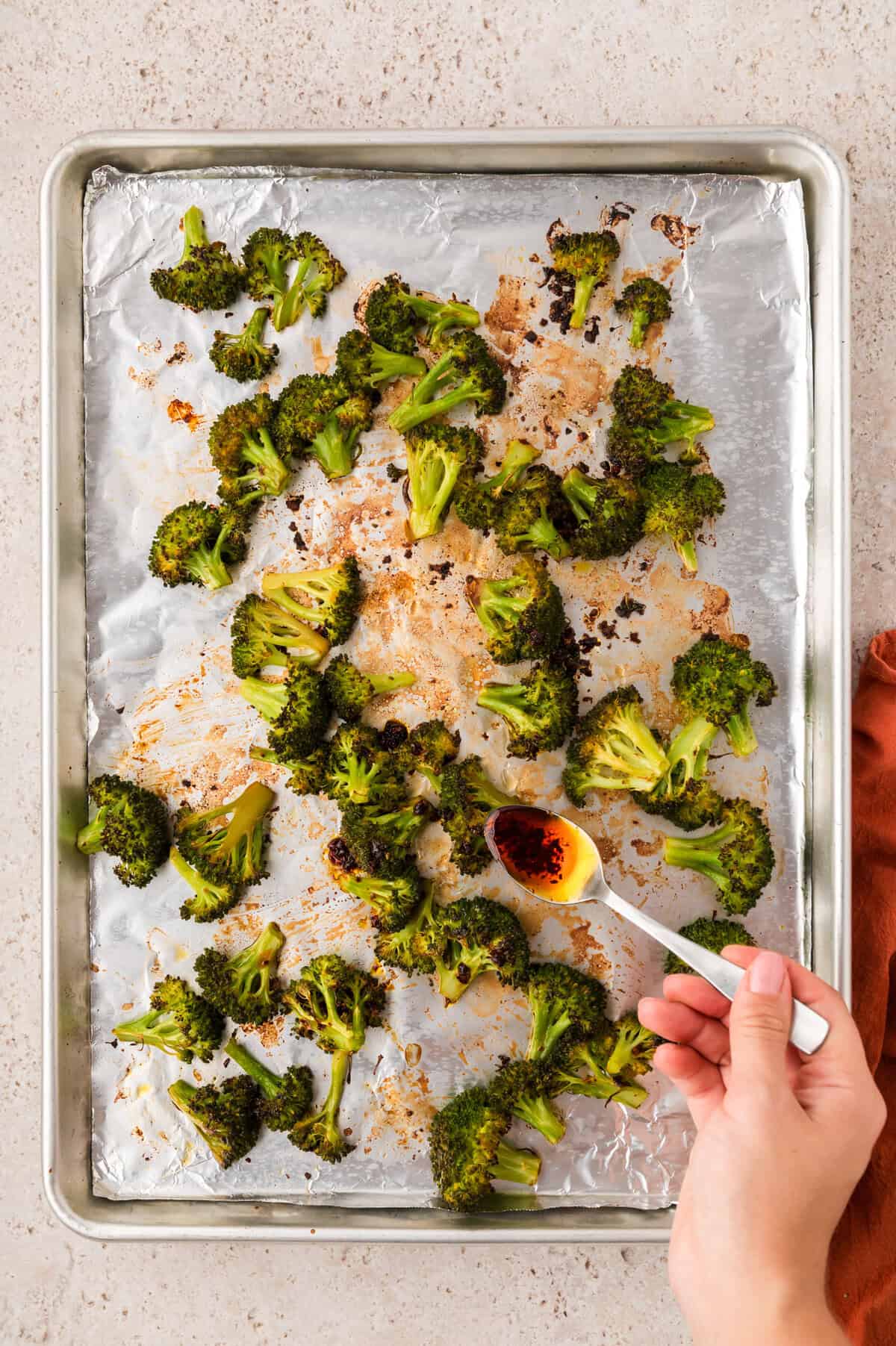 Roasted broccoli being drizzled with sauce.