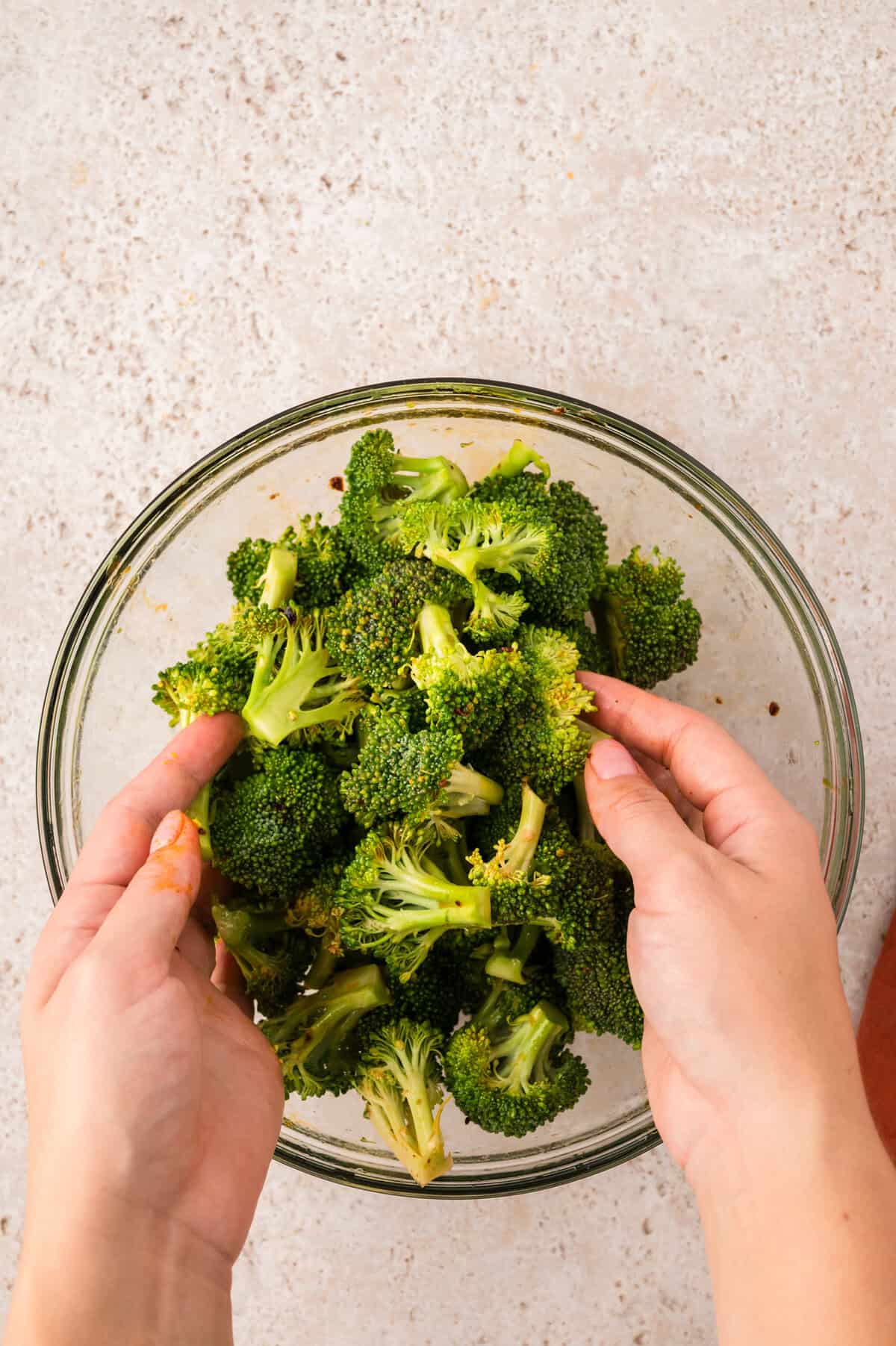 Hands tossing broccoli in soy sauce mixture.