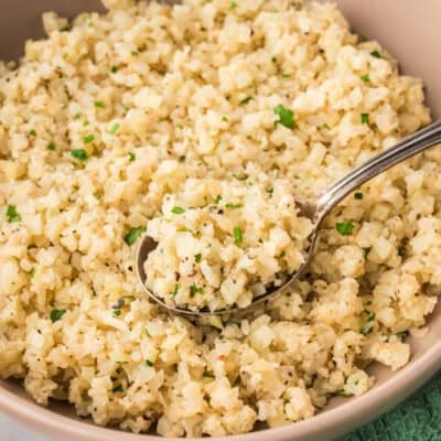 Spoon in a bowl of frozen cauiflower rice with Parmesan and black pepper.