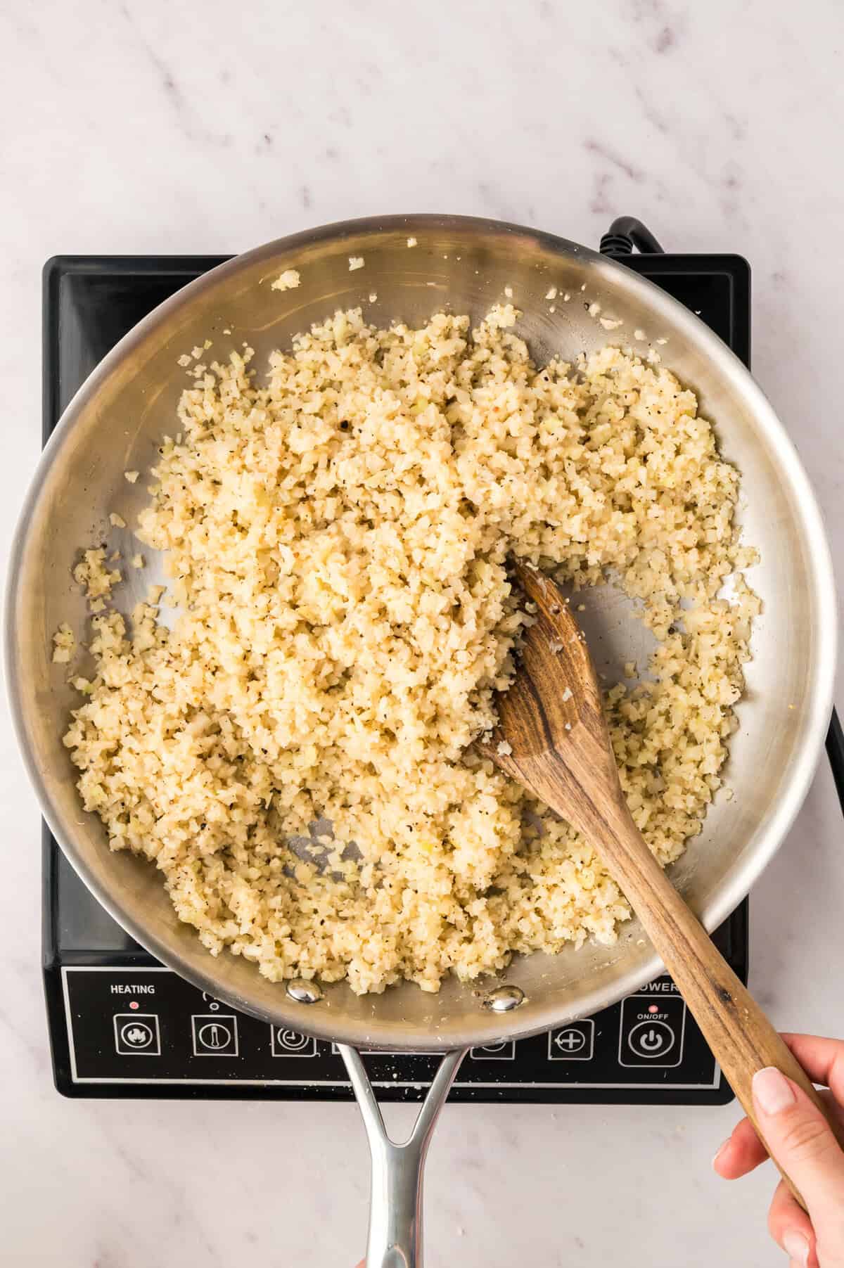 Cacio e pepe cauliflower rice in skillet with wooden spoon.