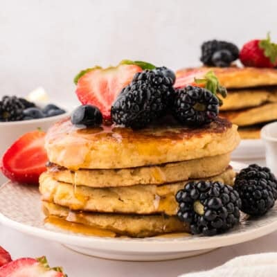Almond flour pancakes stacked on a white plate and topped with fresh fruit.