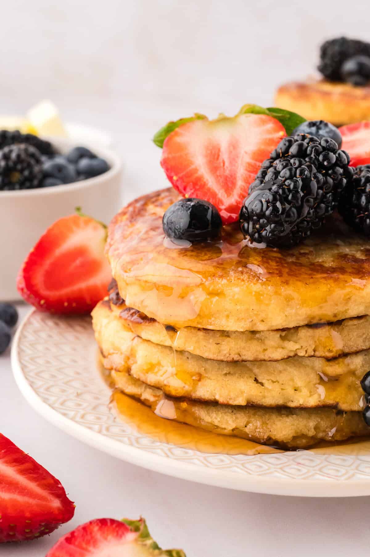 Stack of keto pancakes on a white plate, topped with fruit and syrup.