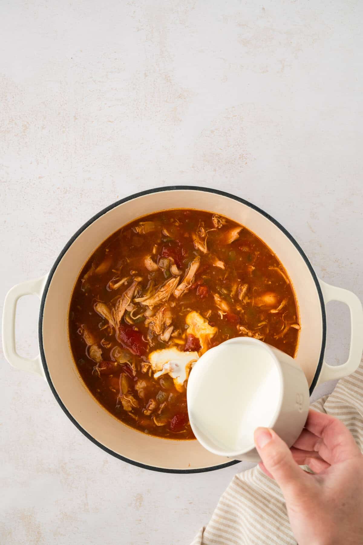 Heavy cream being poured into a pot of buffalo chicken soup.