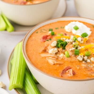 Bowl full of buffalo chicken soup on plate with celery sticks.