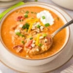 Hand holding a spoonful of buffalo chicken soup over bowl.