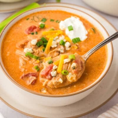 Hand holding a spoonful of buffalo chicken soup over bowl.