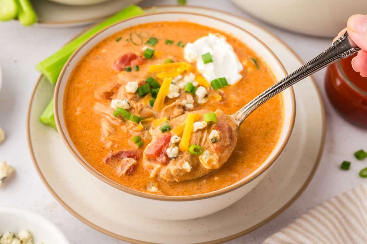 Hand holding a spoonful of buffalo chicken soup over bowl.