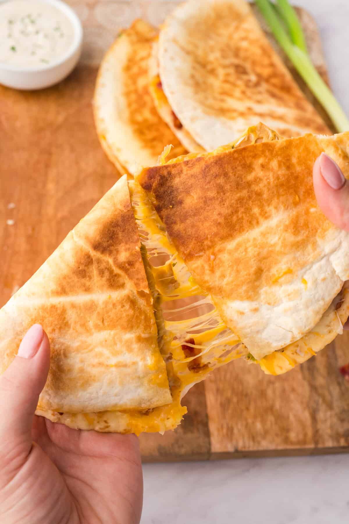 Hands pulling apart a cheesy quesadilla.